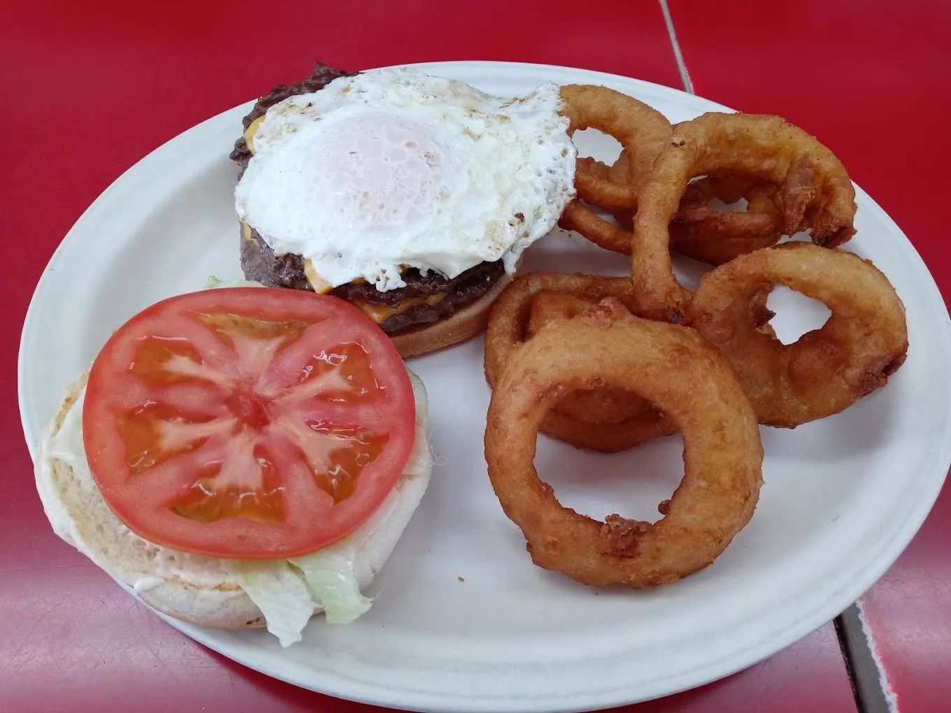 A cheeseburger topped with a fried egg, with tomato, lettuce and a pile of onion rings