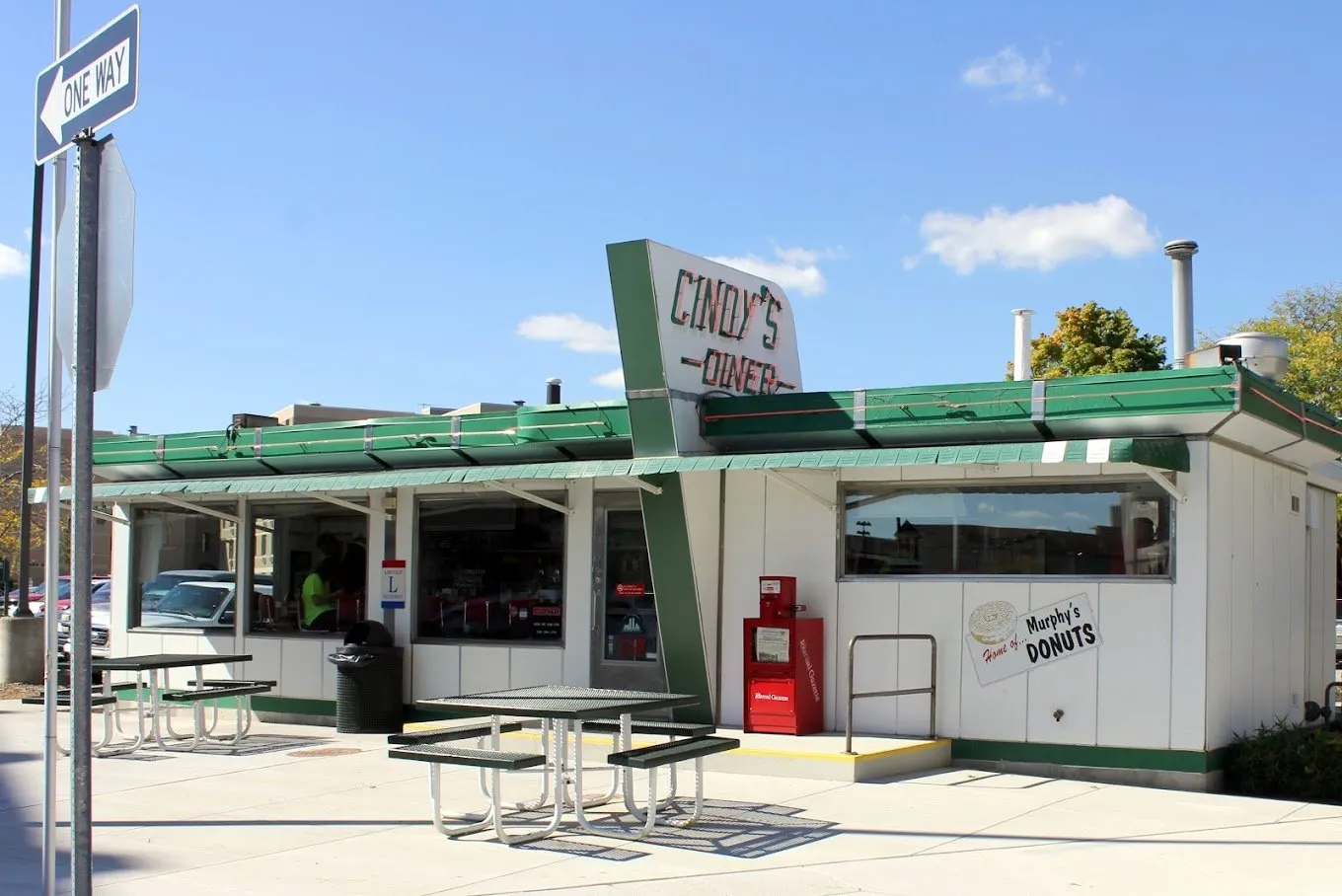 The white diner car with its green awning and angled “Cindy’s Diner” sign, a “Home of Murphy’s Donuts” sign on the side and picnic tables out front